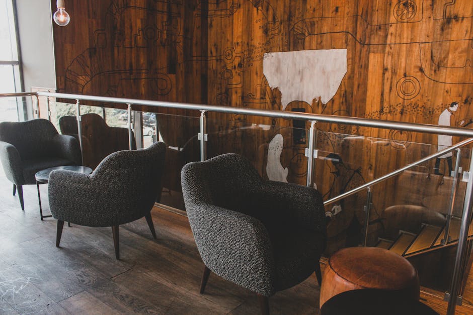 Interior view of a commercial space featuring a row of four upholstered armchairs with dark fabric, arranged along a wooden floor. The chairs are positioned in front of a polished wooden wall with an