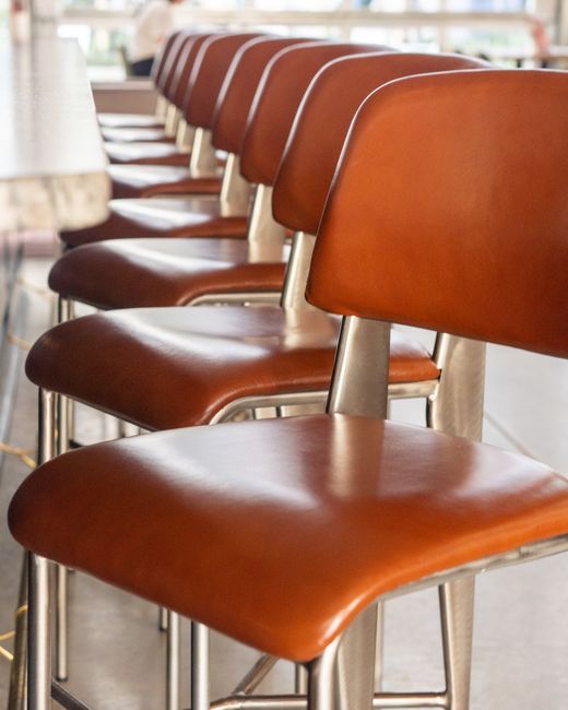 Interior view of a commercial space featuring a row of four upholstered armchairs with dark fabric, arranged along a wooden floor. The chairs are positioned in front of a polished wooden wall with an